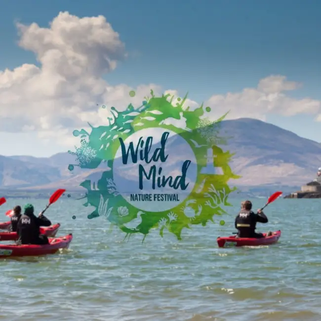 Graphic overlay reading "wild mind nature festival" centers over an image of people kayaking on a lake with mountains in the background on a clear day.