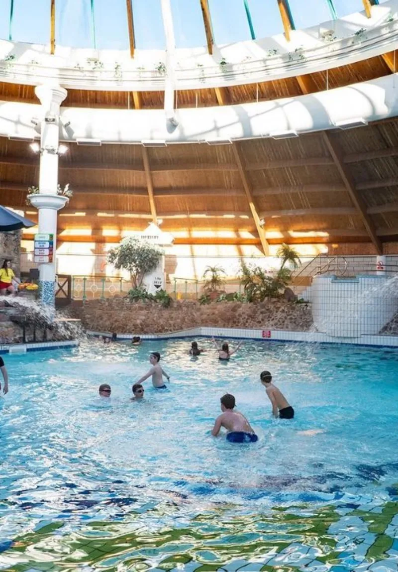 Indoor swimming pool with a wood-paneled ceiling and natural light. People are leisurely enjoying the water.