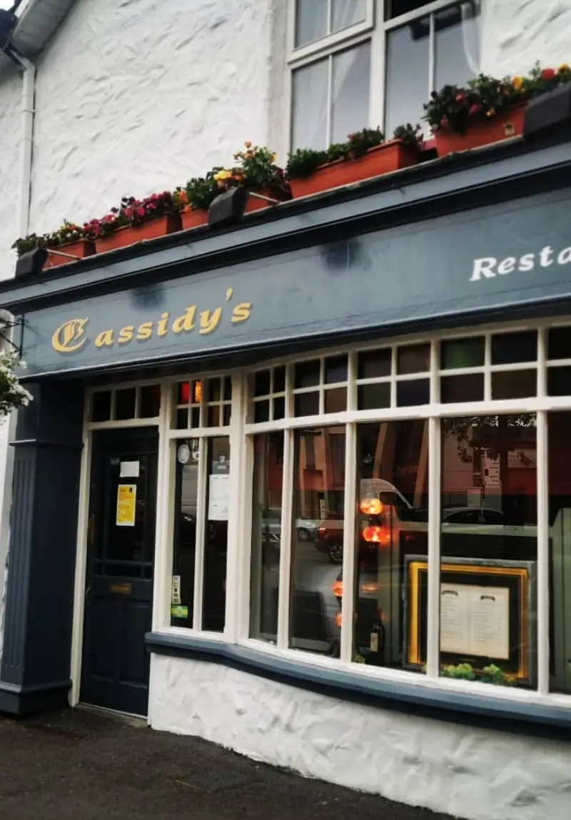 Exterior view of Cassidy's Restaurant, featuring a blue and white facade with window flower boxes and a reflective glass window showcasing interior lights.