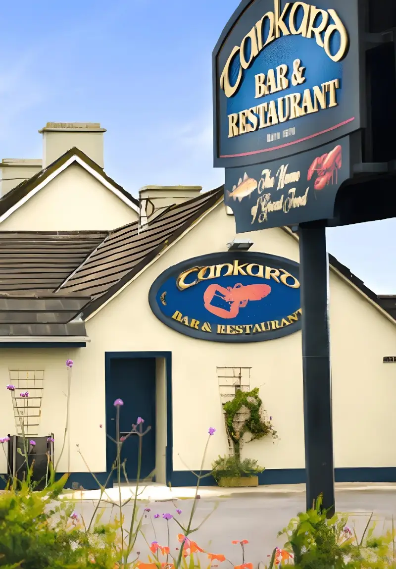 Exterior of the Conkaro Bar & Restaurant with its sign, featuring a whale design, visible on a sunny day beside a white building with blue trim.