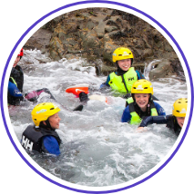 A group of people wearing yellow helmets and safety gear are enjoying a white-water rafting adventure, surrounded by rocks and splashing water. They are smiling and appear to be having fun.